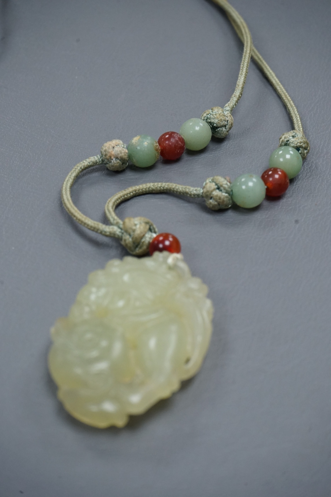 A Chinese carved bowenite jade pendant, on knotted beaded cord, pendant 6cm long.